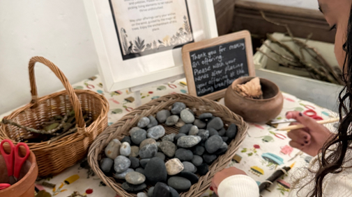 A child takes part in a nature craft activity at Lanhydrock, with baskets of pebbles, twigs and craft materials spread across a table.
